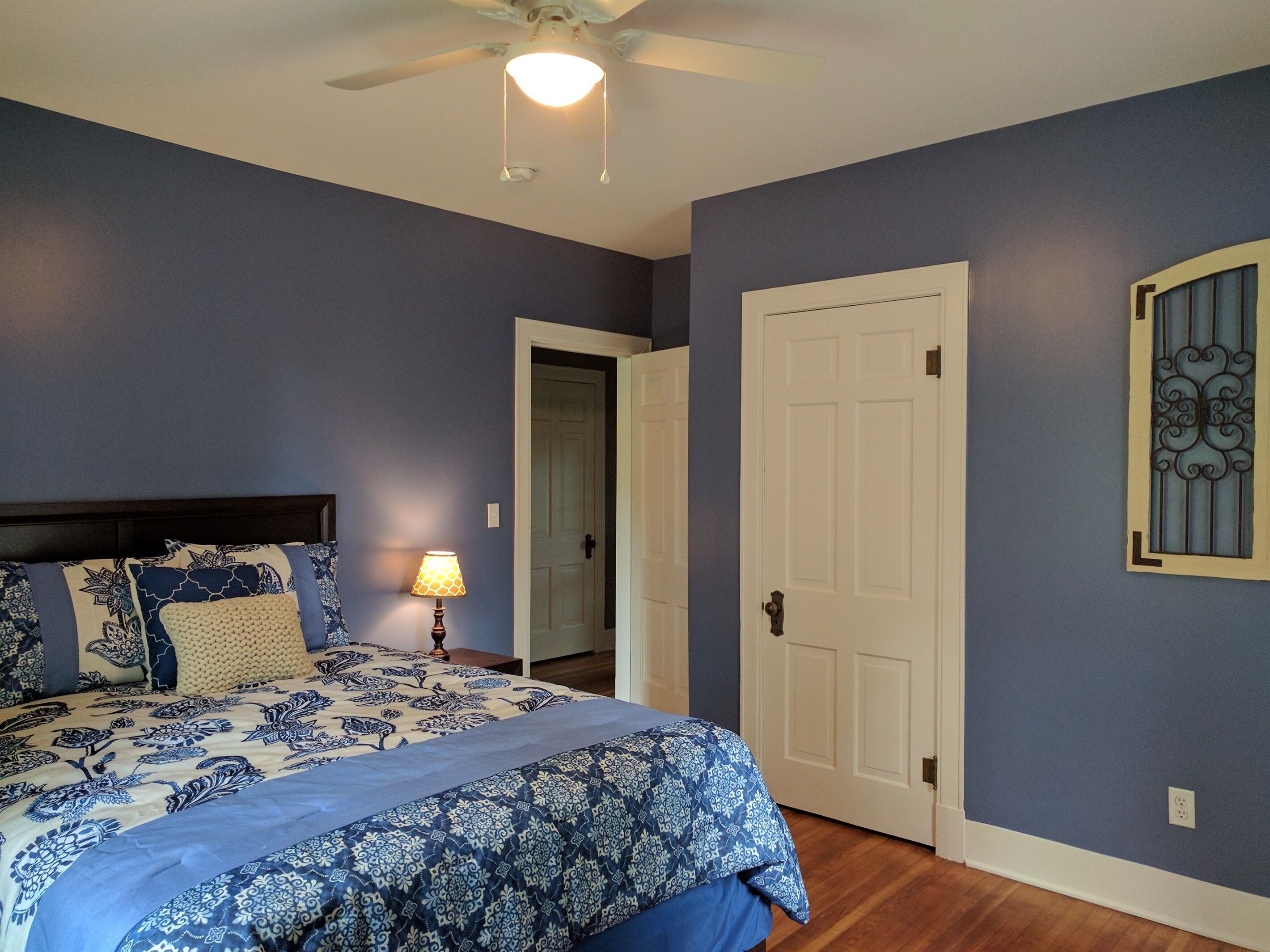 Un dormitorio con cama, mesita de noche, lámpara, puerta y ventilador de techo.