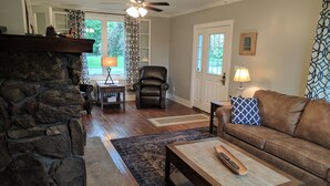 A living room with a stone wall, a brown leather sofa, a wooden coffee table, a black leather chair, and a ceiling fan. - Stonehouse w/ Hot Tub, Walk to GAP Trail & Town (Confluence)