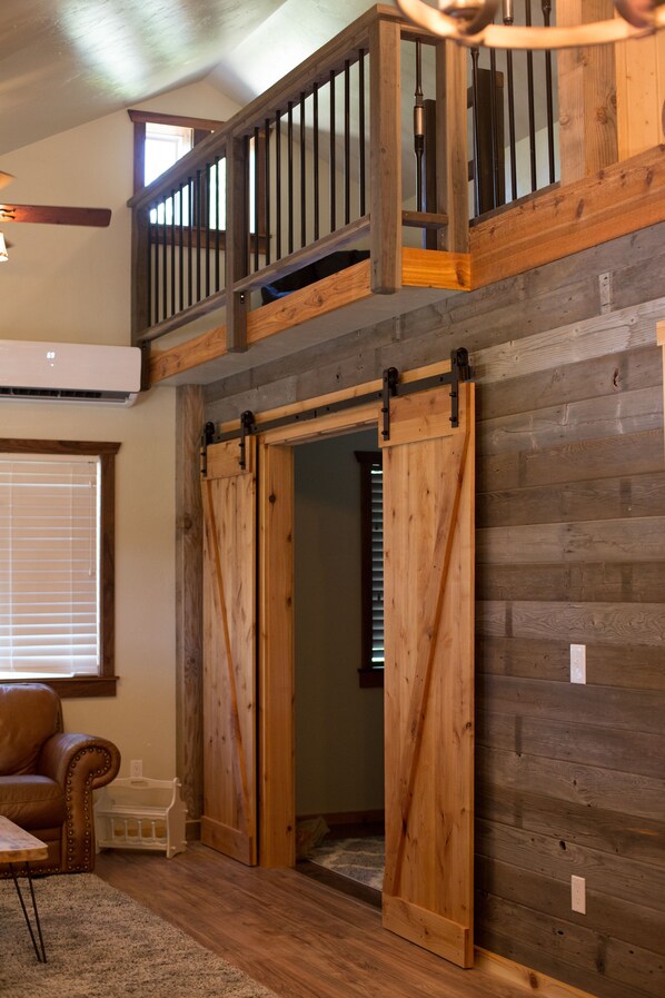 A loft-style room with a wooden staircase, a sliding barn door, and a cozy seating area with a leather chair.