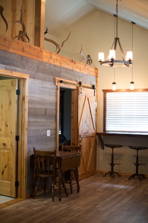 Cozy dining area with a rustic wooden table and chairs near a barn-style door, featuring a chandelier and wooden panel walls.