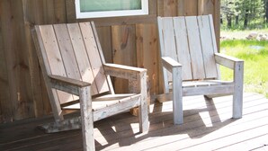 Deux chaises Adirondack en bois sont posées sur une terrasse en bois, avec un mur en bois et une fenêtre en arrière-plan.