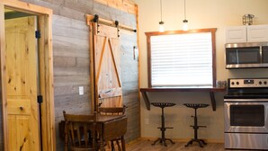 Une cuisine avec des murs en bois, une table à manger avec des chaises, une porte coulissante de style grange, une fenêtre avec des stores et des appareils électroménagers en acier inoxydable.