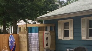 Un'area patio con due poltrone in vimini, un tavolo, una tavola da surf e una tenda decorata.