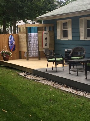 Relax on the patio with a surfboard and wicker chairs, surrounded by a lush lawn and a gravel path.