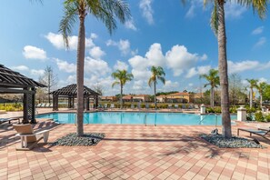 Une piscine entourée de chaises longues et de palmiers, le tout bordé d’une terrasse carrelée.