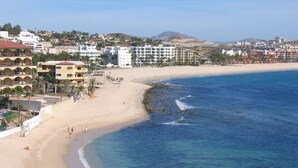 A coastal hotel with multiple balconies, a sandy beach, and a view of the ocean.