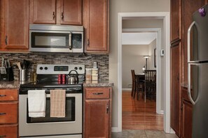 Una cocina con armarios de madera, un microondas de acero inoxidable, una estufa y un refrigerador.