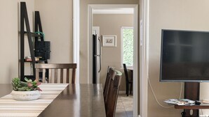 Un área de comedor con una mesa larga, sillas, un televisor y una planta.