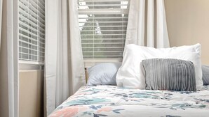 Un dormitorio con cama, cortinas blancas y ventana con persianas.