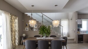 Un moderno comedor con una mesa de madera, seis sillas y una planta en maceta. Se ve una escalera al fondo que sube a un nivel superior.