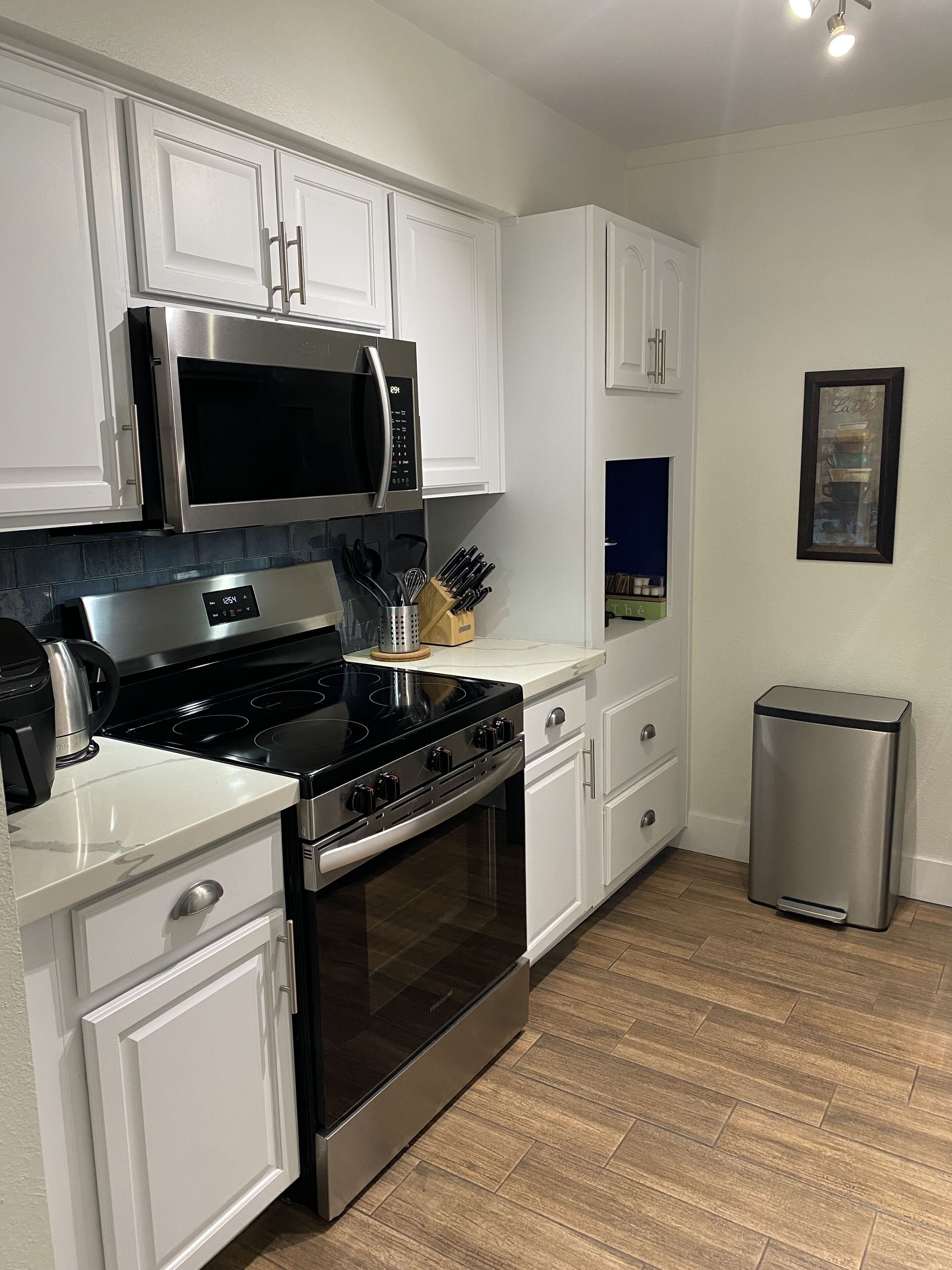 A modern kitchen with white cabinetry, stainless steel appliances, and a herringbone wood floor.