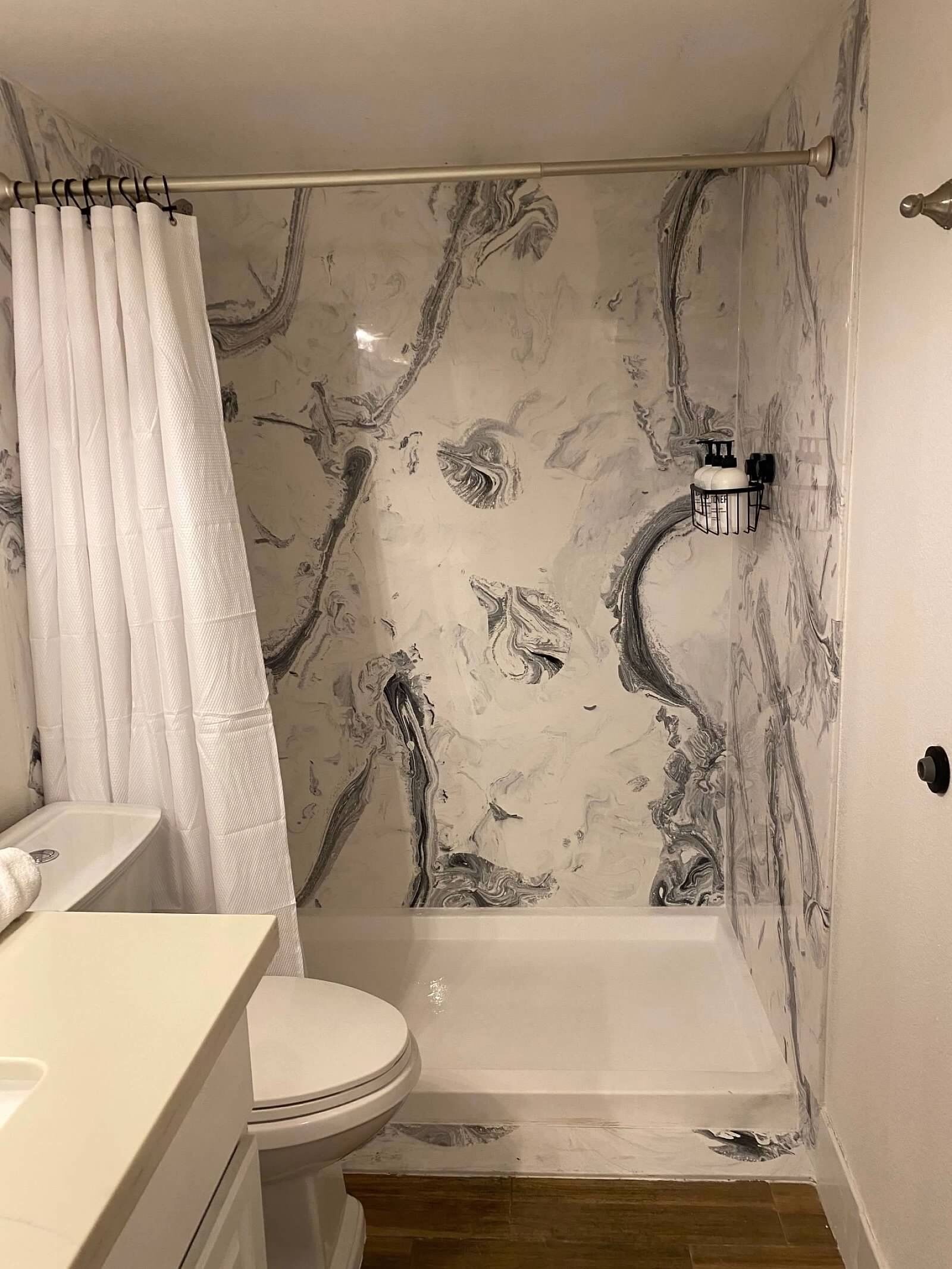 Un baño con pared de mármol, cortina de ducha, inodoro y lavamanos.