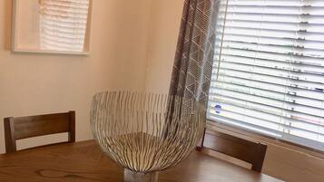 Una mesa de comedor con un centro de mesa tejido, sillas de madera, una lámpara de pared y una ventana con persianas.
