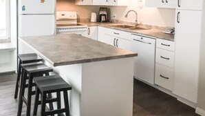 A modern kitchen with white cabinets, a central island with stools, a built-in oven, and a microwave. - Ski In/out For Both Downhill And Cross-country (Vernon)