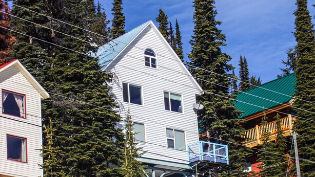 A multi-story building with a sloped roof, surrounded by tall evergreen trees. - Ski In/out For Both Downhill And Cross-country (Vernon)