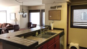 Una cocina con salpicadero de azulejos, un fregadero y un lavavajillas. Hay un cartel de bar en la pared y un taburete pequeño cerca de la ventana.