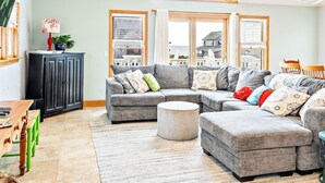 A spacious living room with a high ceiling, large windows, and a cozy seating area. - Semi-Oceanfront, Heated Pool and Hot Tub! (Nags Head)