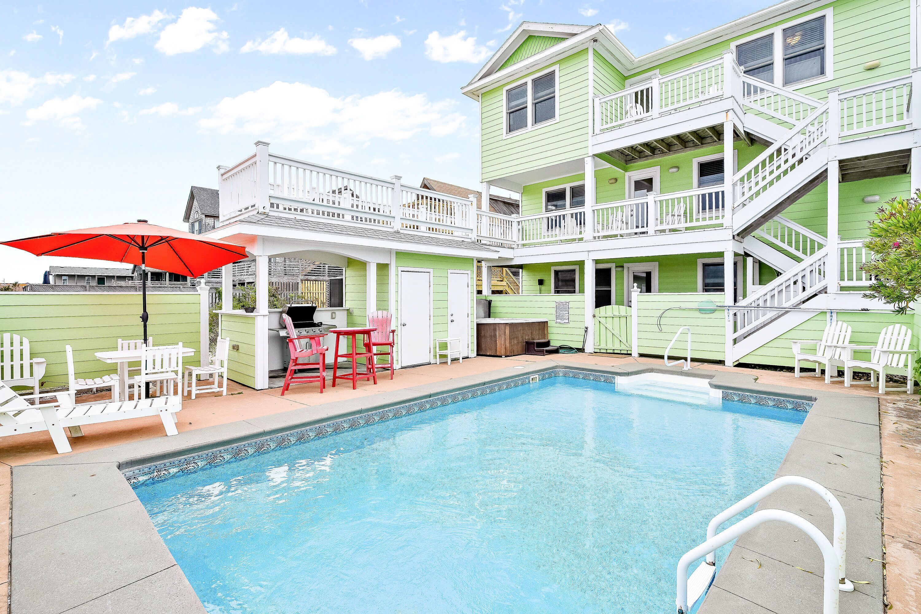 A swimming pool with a white deck, surrounded by a two-story building with a balcony.