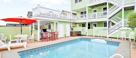 A swimming pool with a white deck, surrounded by a two-story building with a balcony.