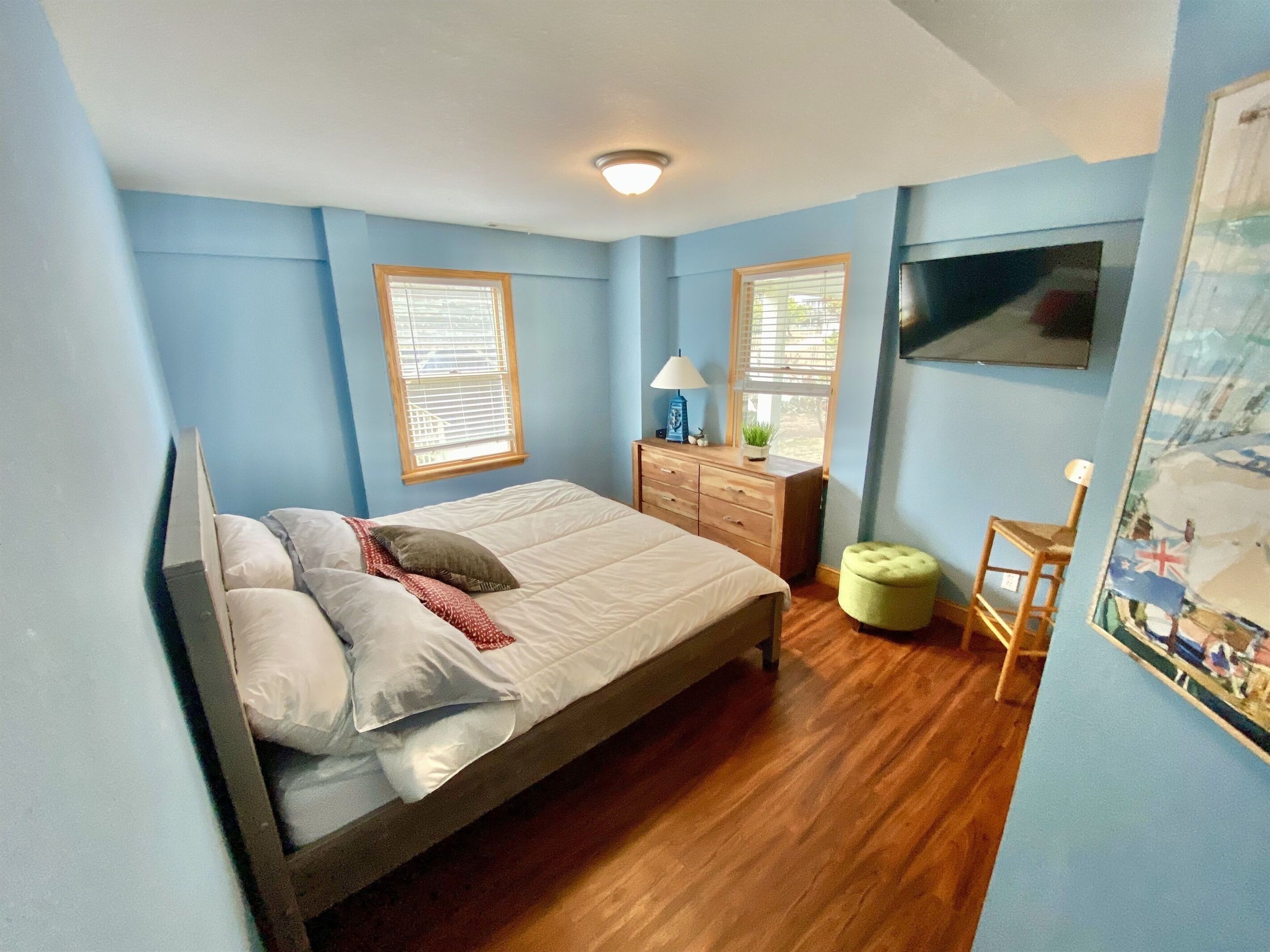 A bedroom with a bed, dresser, nightstand, and a painting on the wall.