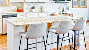 A modern kitchen with white cabinetry, a granite countertop, and a central island with bar stools. - Semi-Oceanfront, Heated Pool and Hot Tub! (Nags Head)