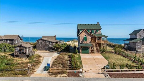 A coastal property with a prominent house featuring a large garage and a balcony overlooking the sea. - Semi-Oceanfront, Heated Pool and Hot Tub! (Nags Head)