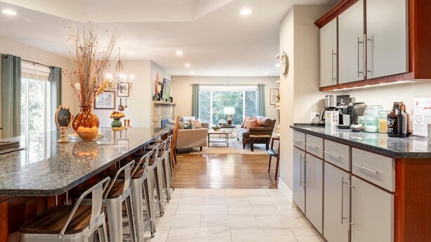 A modern kitchen with a central island, bar stools, and a dining area with a sofa and coffee table.