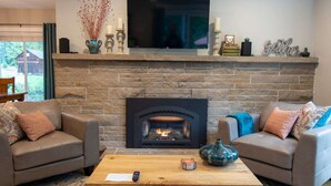 A living room with a stone fireplace, two sofas, a coffee table, and a flat-screen TV mounted above the fireplace.