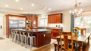 A modern kitchen with a large island, bar stools, wooden cabinets, and a dining table with chairs.