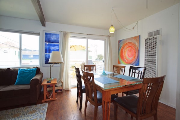 A dining area with a glass-top table, wooden chairs, and a painting on the wall. - Bright, artsy, and cozy home 500 feet from the beach, 500 feet from the river (Aptos)