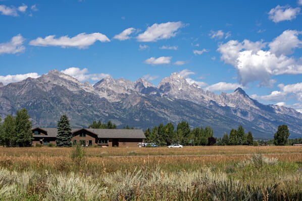 A lodge with a mountain backdrop, featuring a large open field in the foreground and a clear sky.