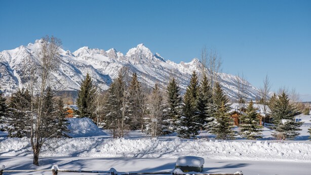 A snow-covered landscape with mountains in the background, a few trees, and a building with a snow-covered roof. - Townhouse near GTNP and Yellowstone -Spectacular Views - 2-3 bed-2 bath (Jackson)