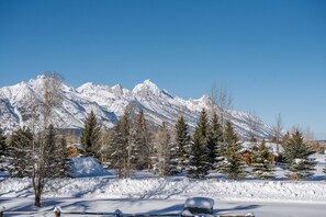 A snow-covered landscape with mountains in the background, a few trees, and a building with a snow-covered roof.