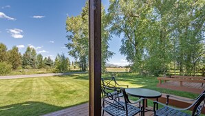 A wooden deck with outdoor furniture, a picnic table, and a view of a grassy area with trees and a distant mountain range. - Townhouse near GTNP and Yellowstone -Spectacular Views - 2-3 bed-2 bath (Jackson)