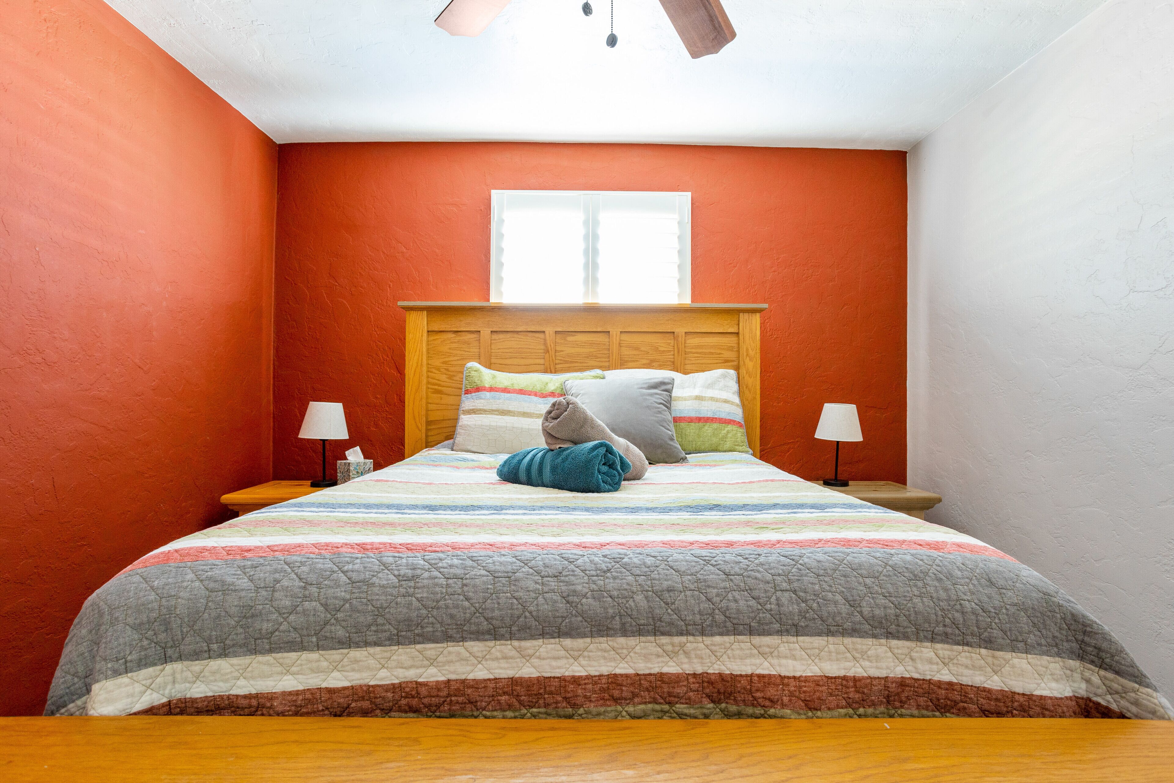 A bedroom with a wooden headboard, a striped bedspread, and two bedside lamps.