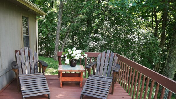 A wooden deck with two chairs and a small table, surrounded by a wooden railing and lush greenery.