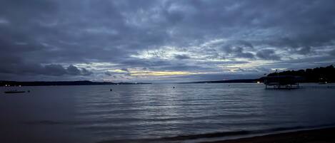 A beach with calm waters, a distant shoreline, and a cloudy sky.