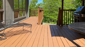 Une terrasse en bois avec un barbecue et du mobilier d’extérieur, offrant une vue sur un paysage verdoyant et luxuriant.