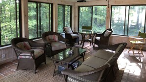 Une pièce spacieuse avec de grandes fenêtres, des meubles en osier, une table en verre et un ventilateur de plafond.
