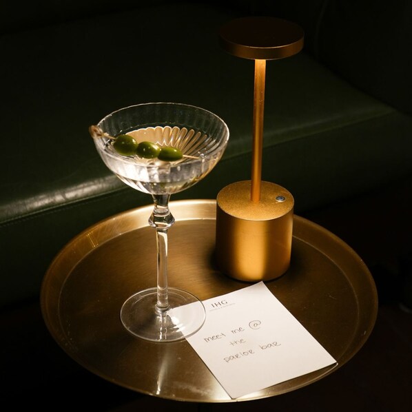 Una copa de martini con aceitunas en una bandeja, un objeto dorado y una nota sobre una mesa.