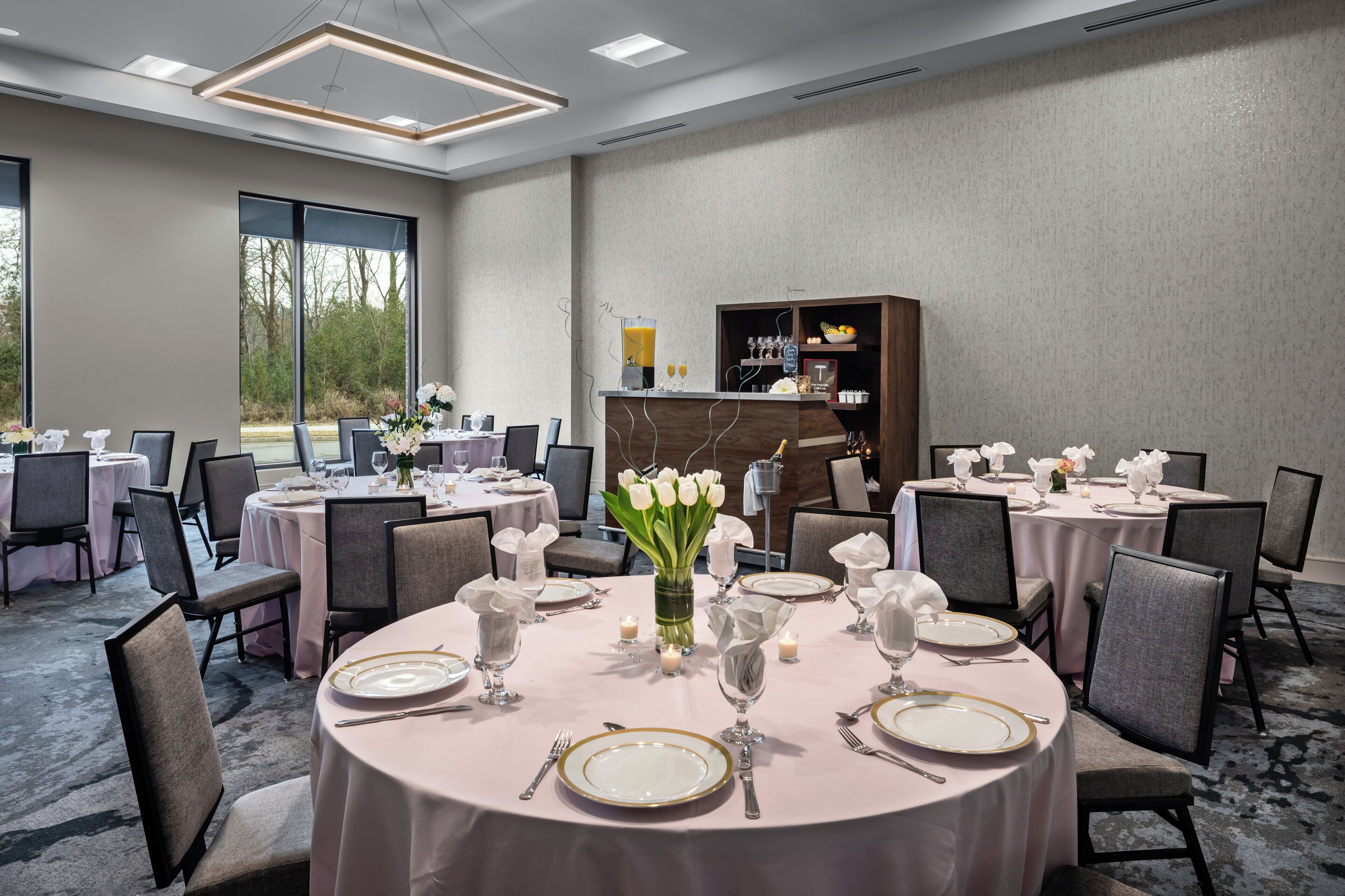Ein Restaurantbereich eines Hotels mit runden Tischen, gedeckten Plätzen, Stühlen und einer Speiseauslage im Hintergrund.