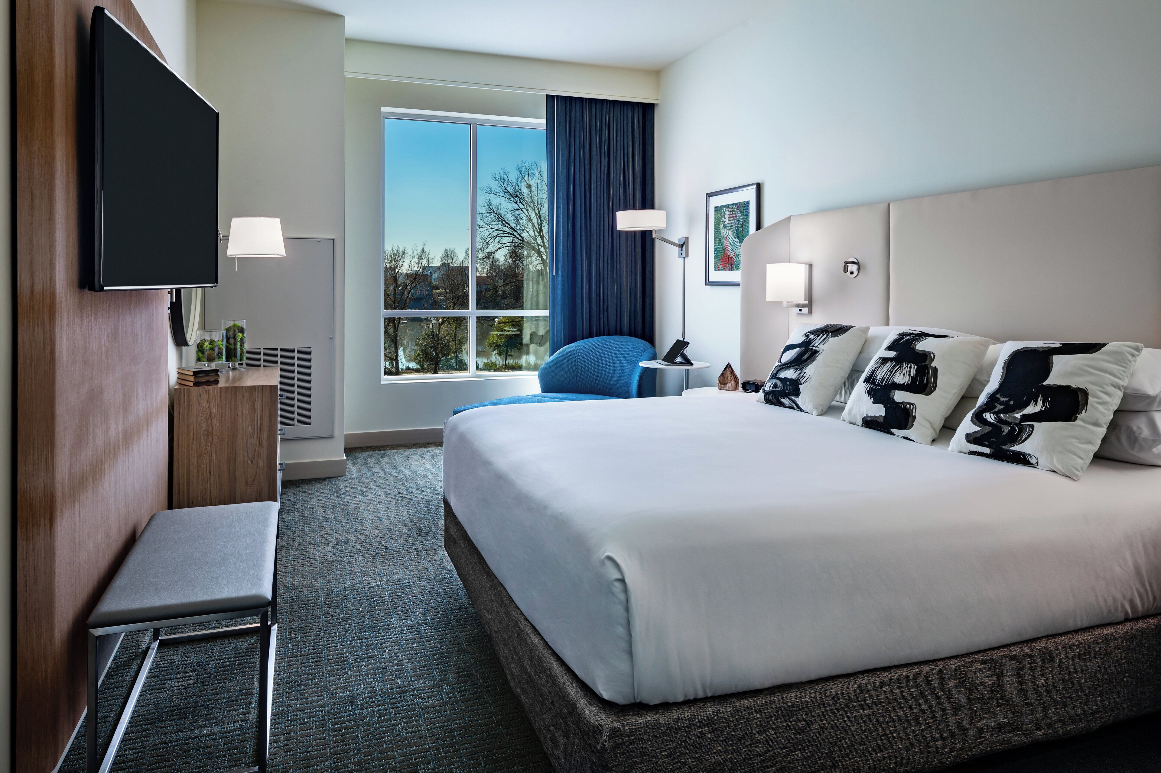 Une chambre d’hôtel équipée d’un lit, d’un bureau, d’une chaise, d’une télévision et d’une fenêtre donnant sur un paysage agréable.