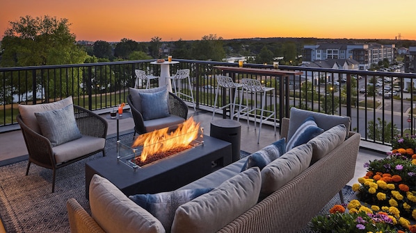 A balcony with a fire pit, outdoor seating, and a view of the cityscape at sunset. - Crowne Plaza North Augusta by IHG (North Augusta)