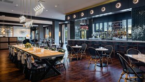 A modern restaurant with wooden flooring, a bar area with a wine rack, and a seating arrangement with tables and chairs.