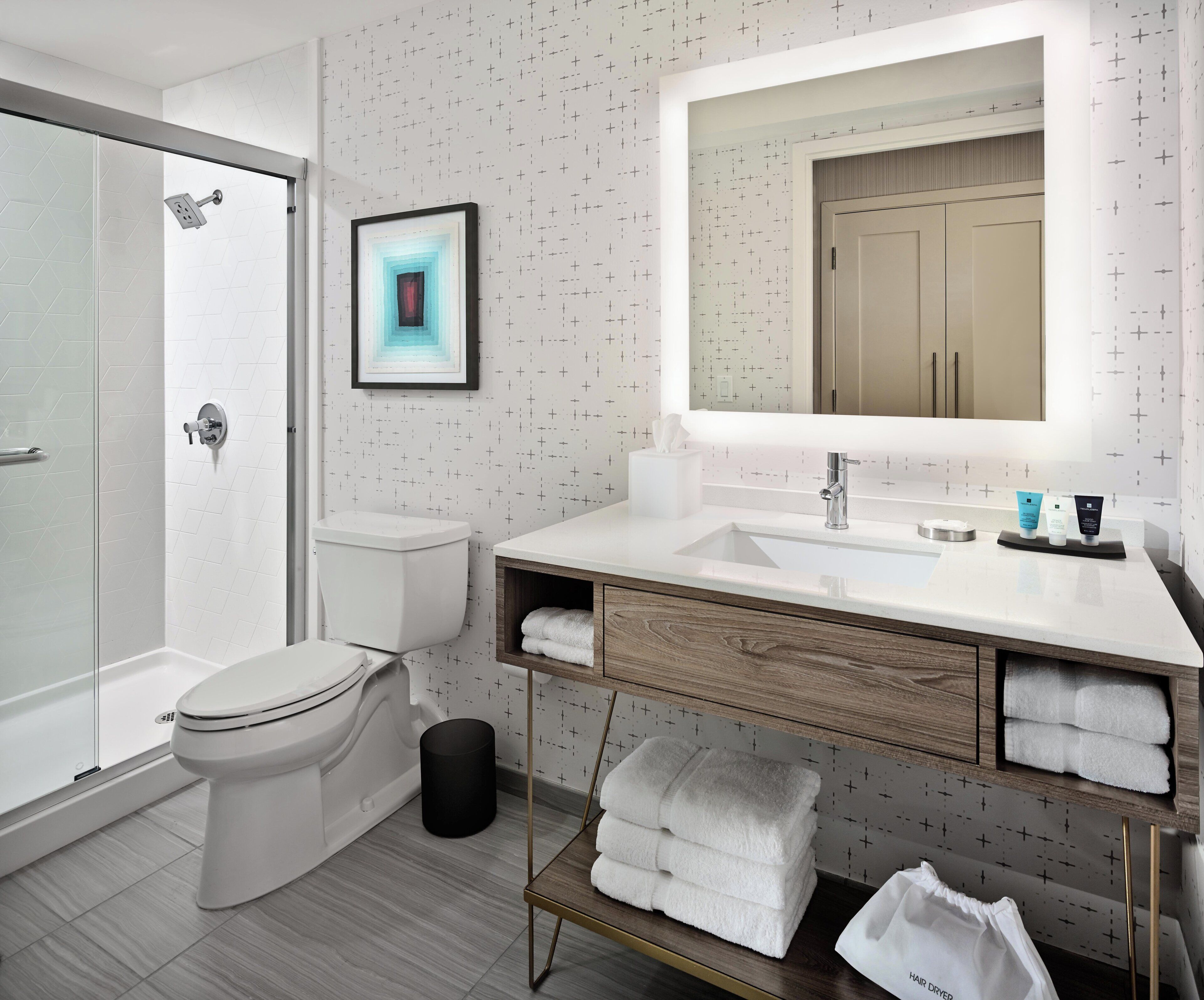 A modern bathroom with a glass shower enclosure, a white toilet, a vanity with a large mirror, and neatly folded towels.