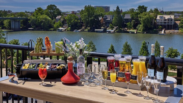 A table with a variety of food and drinks, overlooking a lake with buildings in the background.