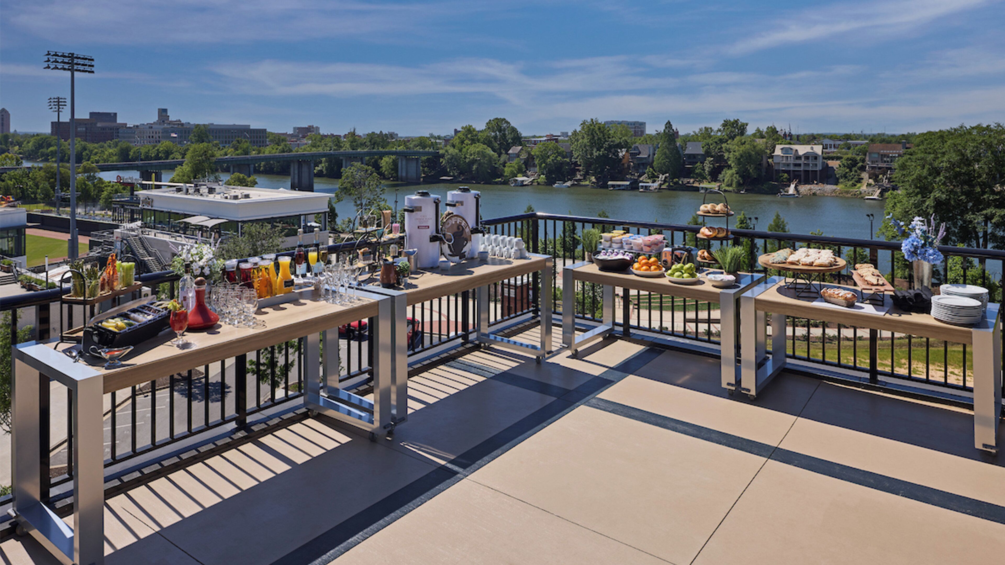 A rooftop terrace with dining tables, a view of a river, and a bridge in the background.