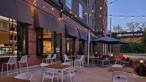 An outdoor seating area with tables and chairs, a brick building facade, and a sign reading 'CROWNE PLAZA'. - Crowne Plaza North Augusta by IHG (North Augusta)