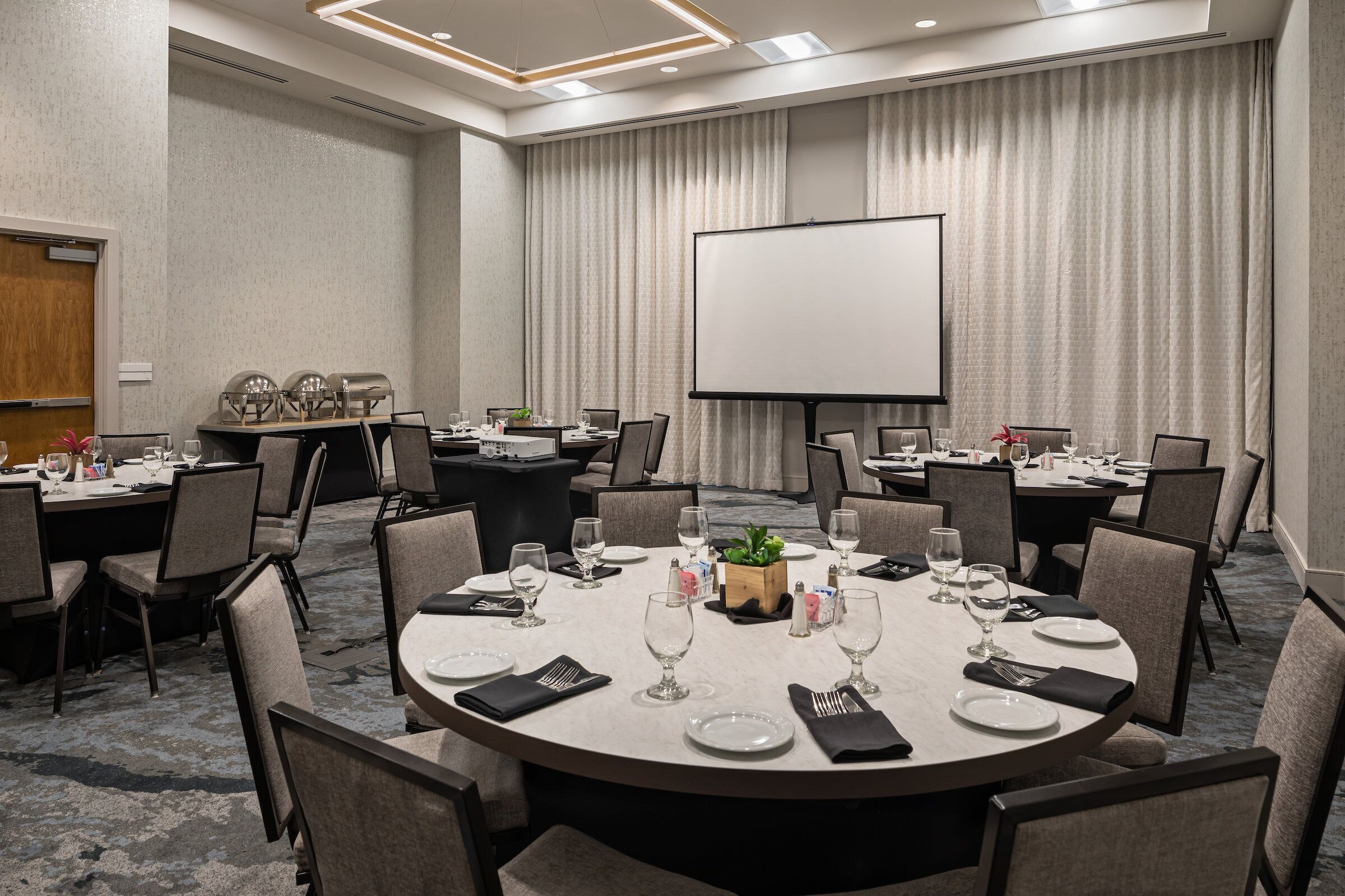 A conference room with round tables, chairs, a projector screen, and a whiteboard.