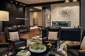 A modern lobby with leather chairs, a fireplace, and a large plant centerpiece. - Crowne Plaza North Augusta by IHG (North Augusta)
